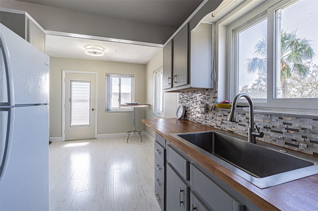 kitchen with gray cabinetry, a sink, baseboards, freestanding refrigerator, and decorative backsplash