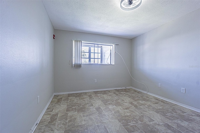 unfurnished room featuring stone finish floor, baseboards, and a textured ceiling