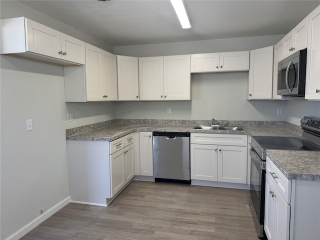 kitchen featuring stainless steel appliances, wood finished floors, a sink, and white cabinetry