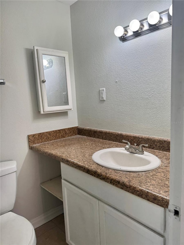 half bathroom featuring tile patterned flooring, baseboards, vanity, and toilet