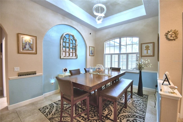 dining space featuring arched walkways, a tray ceiling, light tile patterned floors, and baseboards