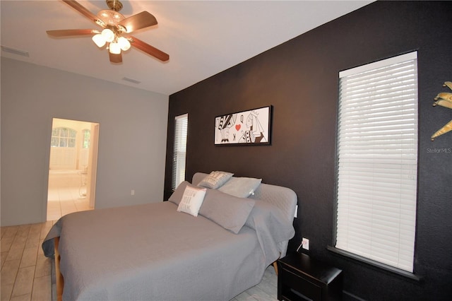 bedroom featuring light wood-style floors, ceiling fan, visible vents, and connected bathroom