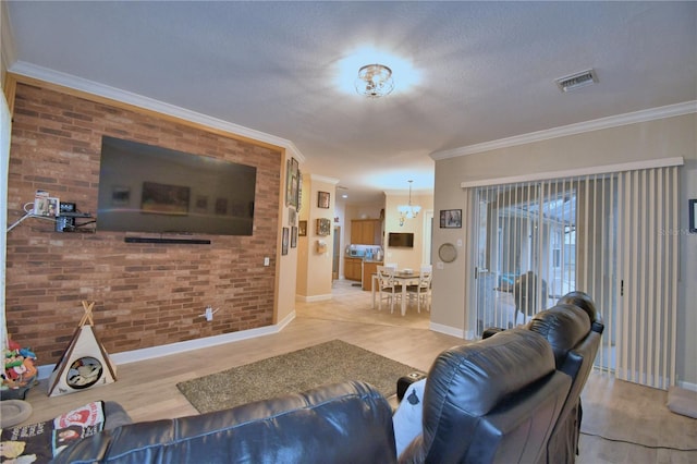 living area with crown molding, visible vents, an inviting chandelier, brick wall, and wood finished floors