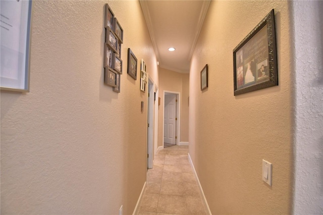 corridor with light tile patterned floors, a textured wall, ornamental molding, and baseboards