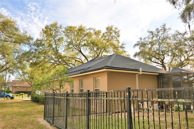 view of home's exterior featuring roof with shingles, fence, a lawn, and stucco siding