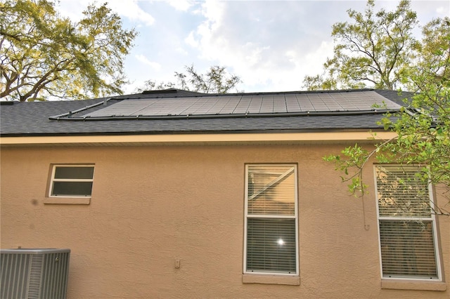 view of property exterior featuring roof with shingles, stucco siding, roof mounted solar panels, and central air condition unit