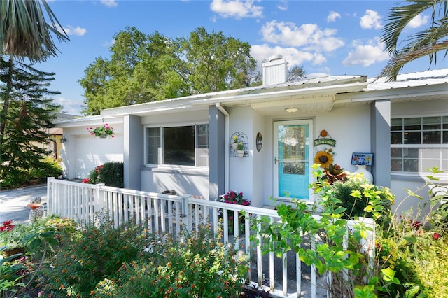 property entrance with a garage, fence, a chimney, and stucco siding