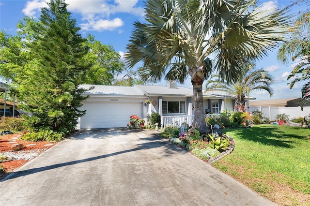 single story home with a porch, concrete driveway, an attached garage, metal roof, and a front lawn