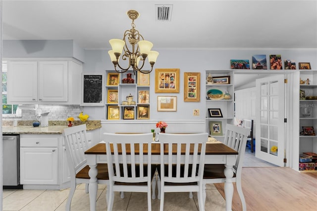 dining area with light tile patterned flooring, visible vents, wainscoting, an inviting chandelier, and crown molding