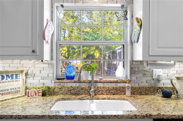 interior details with light stone counters, backsplash, a sink, and white cabinets