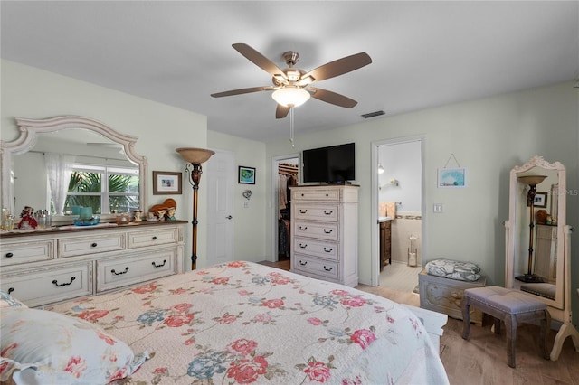 bedroom featuring ensuite bath, visible vents, a ceiling fan, light wood finished floors, and a walk in closet