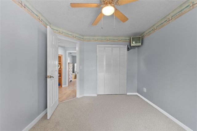 unfurnished bedroom with a closet, carpet flooring, ceiling fan, a textured ceiling, and baseboards