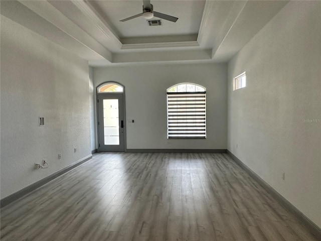 interior space featuring a raised ceiling, visible vents, ceiling fan, wood finished floors, and baseboards