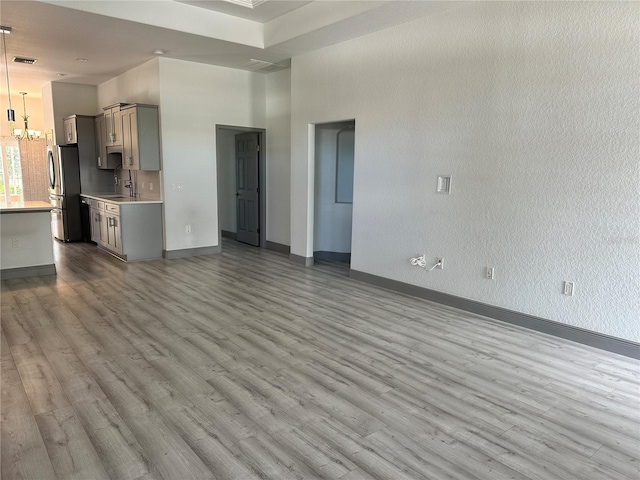 unfurnished living room with a towering ceiling, a sink, wood finished floors, a chandelier, and baseboards