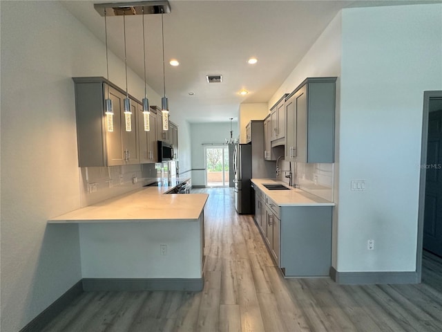 kitchen with gray cabinetry, a sink, light countertops, appliances with stainless steel finishes, and decorative backsplash