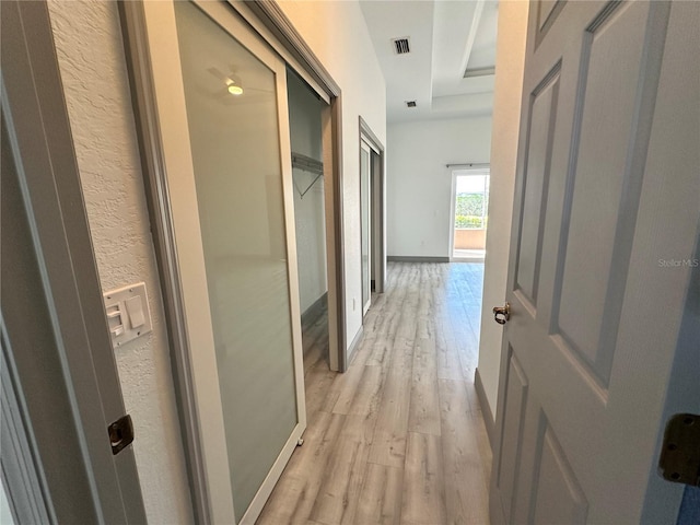 corridor with baseboards, visible vents, and light wood finished floors