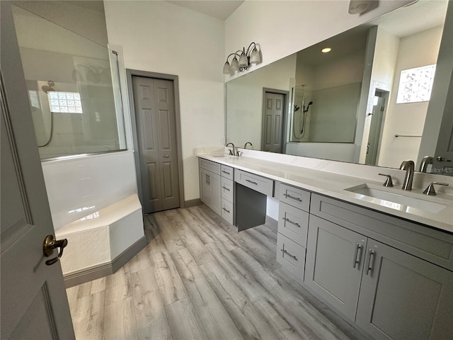 bathroom featuring double vanity, baseboards, wood finished floors, walk in shower, and a sink