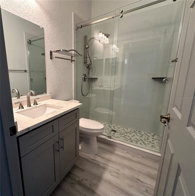 full bath featuring toilet, a stall shower, wood finished floors, and a textured wall