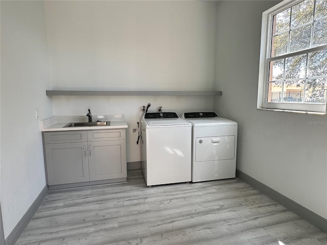 laundry room featuring cabinet space, baseboards, light wood-style flooring, washer and dryer, and a sink