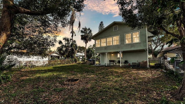 back of house at dusk featuring an outdoor fire pit, a lawn, a fenced backyard, and a patio