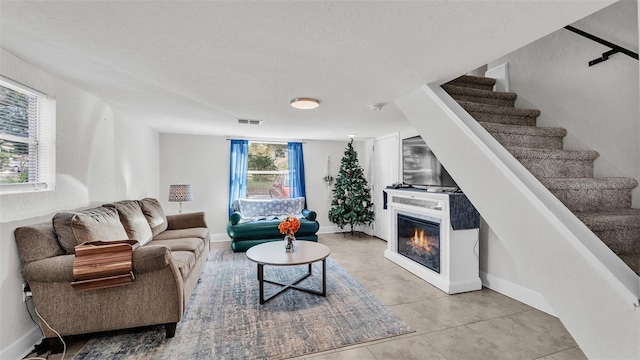 living area featuring stairs, a glass covered fireplace, visible vents, and baseboards