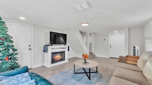 living room featuring baseboards, visible vents, a glass covered fireplace, stairway, and tile patterned flooring