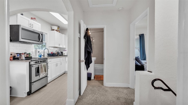 kitchen featuring white cabinetry, stainless steel appliances, decorative backsplash, and light colored carpet