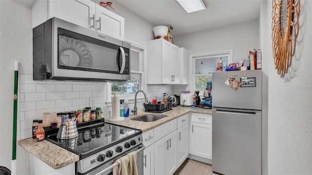 kitchen featuring a sink, white cabinets, appliances with stainless steel finishes, decorative backsplash, and light stone countertops