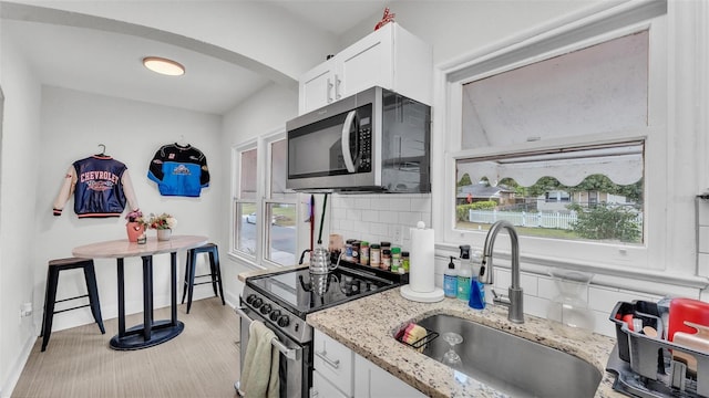 kitchen with white cabinets, decorative backsplash, light stone counters, stainless steel appliances, and a sink