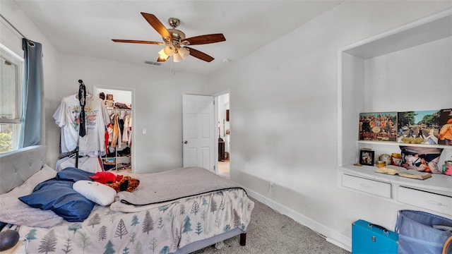 bedroom featuring carpet floors, a ceiling fan, visible vents, baseboards, and a walk in closet