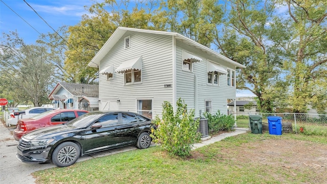 view of property exterior with a lawn, fence, and cooling unit