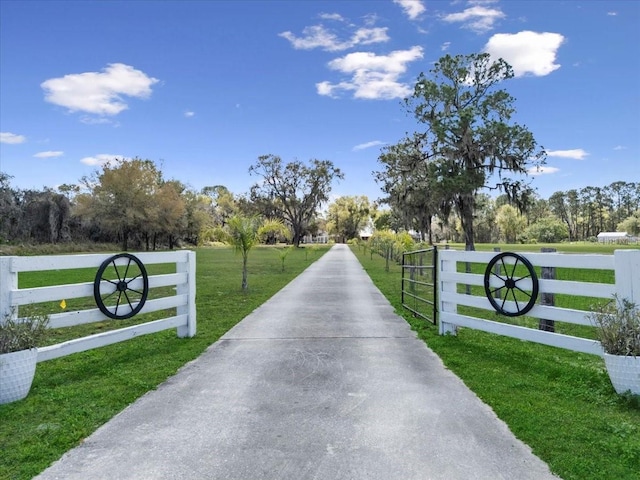 view of gate featuring a rural view, a lawn, and fence