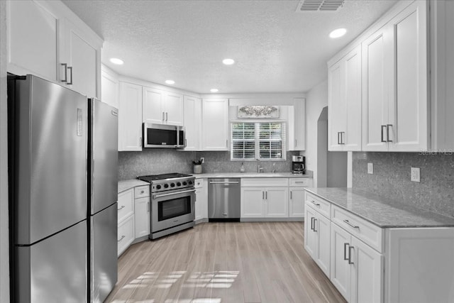 kitchen featuring visible vents, appliances with stainless steel finishes, light wood-style floors, white cabinets, and a sink