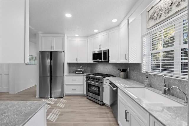 kitchen featuring light stone counters, stainless steel appliances, a sink, white cabinets, and decorative backsplash