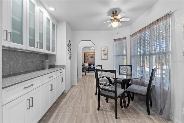 dining space with arched walkways, ceiling fan, wood finish floors, and baseboards