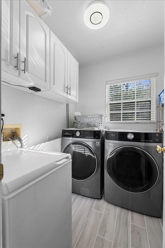 clothes washing area featuring wood finish floors, cabinet space, and washing machine and clothes dryer