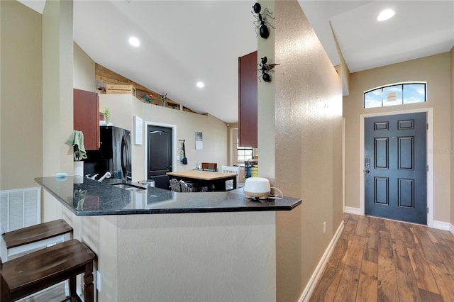 kitchen with recessed lighting, freestanding refrigerator, vaulted ceiling, wood finished floors, and a peninsula