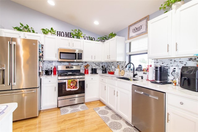 kitchen with vaulted ceiling, light wood-style flooring, appliances with stainless steel finishes, white cabinetry, and a sink