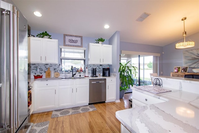 kitchen featuring light stone countertops, stainless steel appliances, light wood-style floors, hanging light fixtures, and white cabinetry