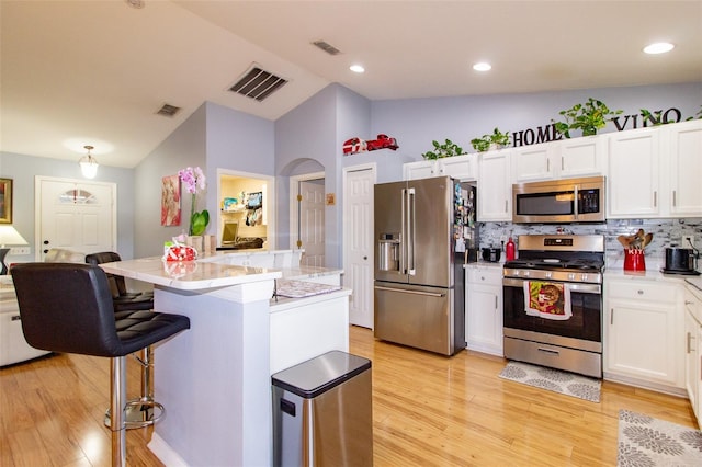 kitchen featuring stainless steel appliances, lofted ceiling, a breakfast bar, and white cabinetry