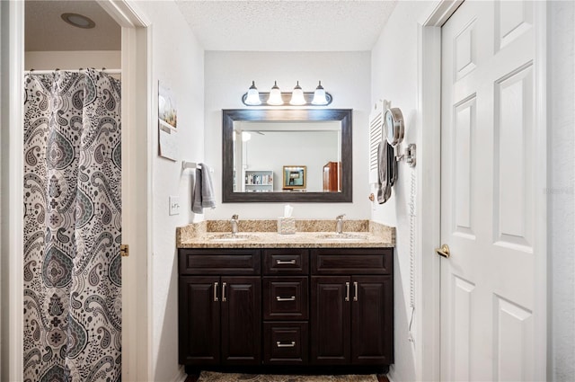 full bathroom with a textured ceiling, double vanity, and a sink