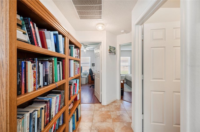 hallway with a textured ceiling, tile patterned flooring, and visible vents