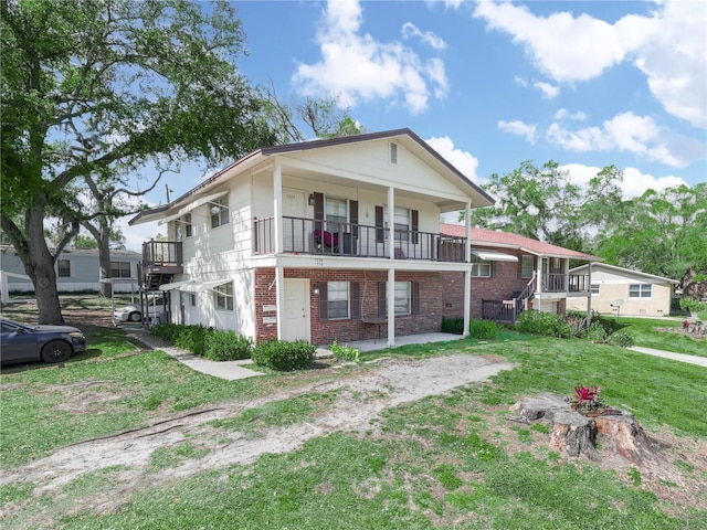 view of front facade featuring a balcony, a front lawn, and brick siding