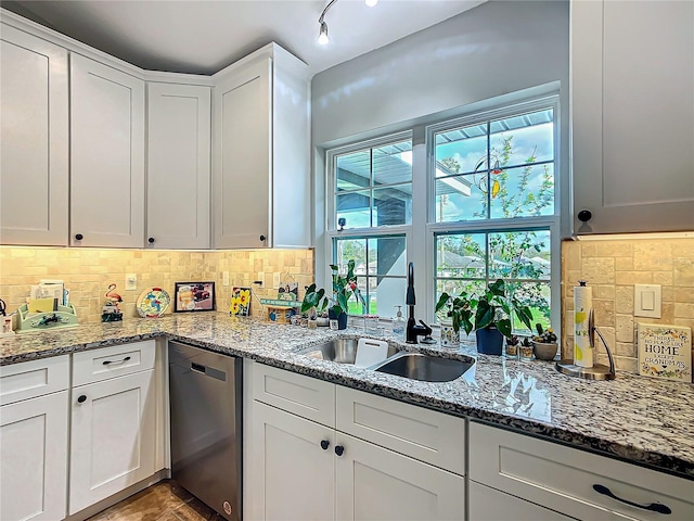 kitchen with stainless steel dishwasher, stone countertops, a sink, and decorative backsplash