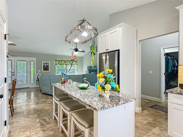 kitchen with light stone countertops, white cabinets, open floor plan, stainless steel refrigerator, and a center island