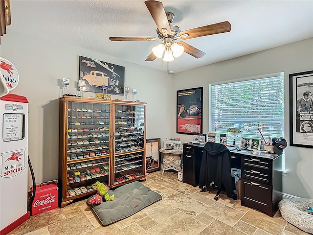 office with a ceiling fan, stone finish floor, a textured ceiling, and baseboards