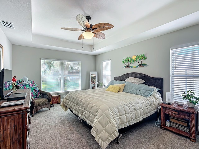 bedroom with carpet floors, a tray ceiling, visible vents, and ceiling fan