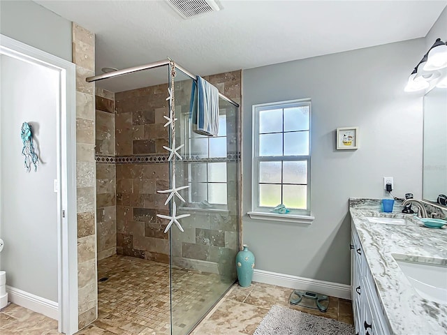 bathroom with visible vents, a tile shower, a sink, and baseboards