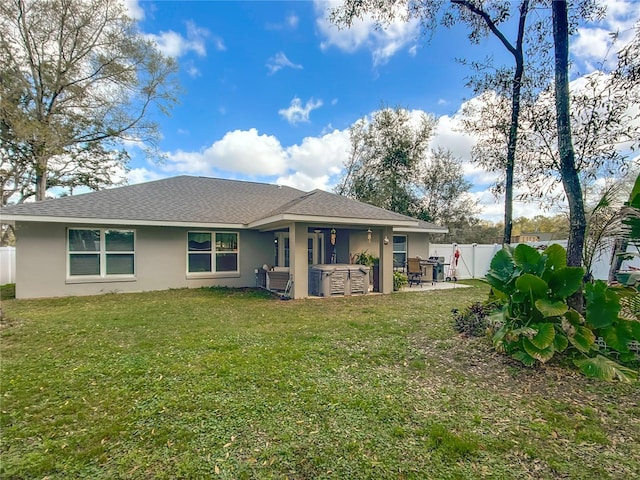 back of house with a hot tub, a fenced backyard, a yard, a patio area, and stucco siding