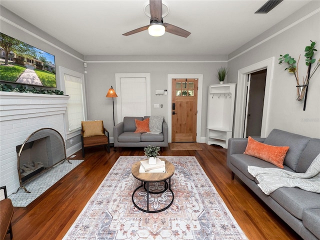 living area featuring ceiling fan, a fireplace, visible vents, baseboards, and dark wood finished floors